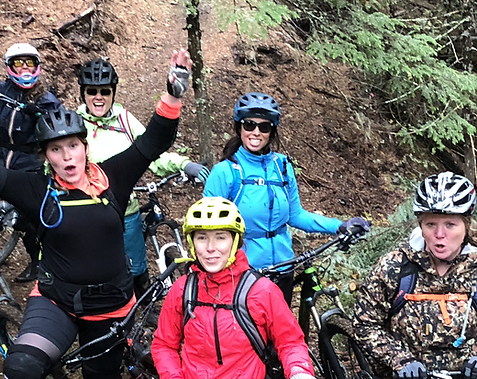 A group of mountain bikers in biking gear, jackets and helmets smile and pose while in a BC forest.